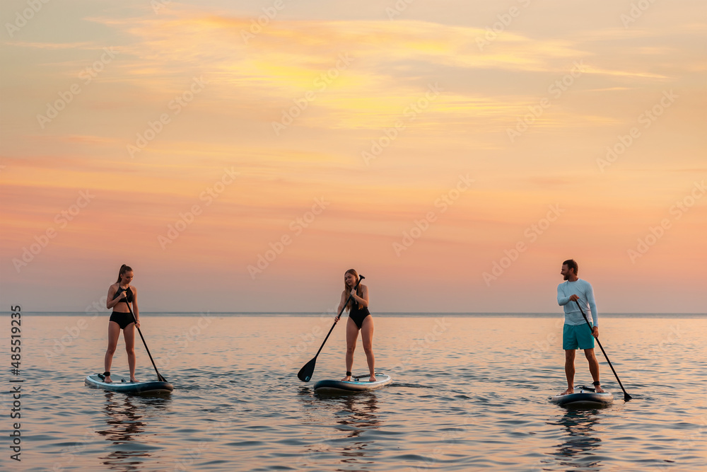 Group of caucasian people swimming on a sup boards at the ocean. Surfing with friends at the vacation. Summer sport activity. Copy space