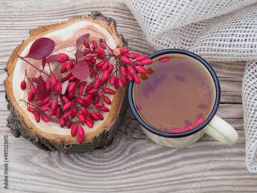 Berries and leaves of the useful berberis plant and a tea in a mug, napkin on a wooden table, top view, flat layout. Seasonal red barberry fruit and drinks for use in medicine and food