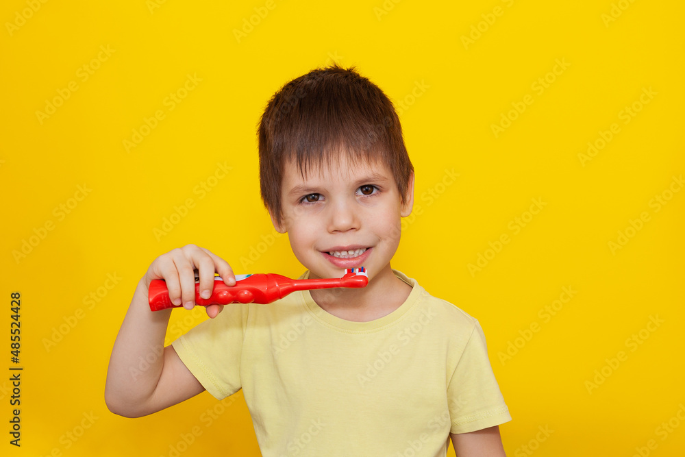 Happy toddler boy brushing his teeth with a toothbrush on a yellow background. Health care, oral hygiene. Happy toddler boy brushing his teeth with a toothbrush on a yellow background. Health care, oral hygiene.