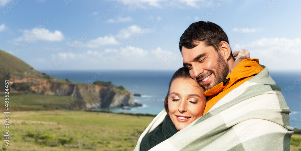 travel, tourism and love concept - happy smiling couple in warm blanket over big sur coast in california background