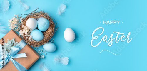 Wallpaper Mural A nest with Easter eggs, a gift and feathers on a blue background