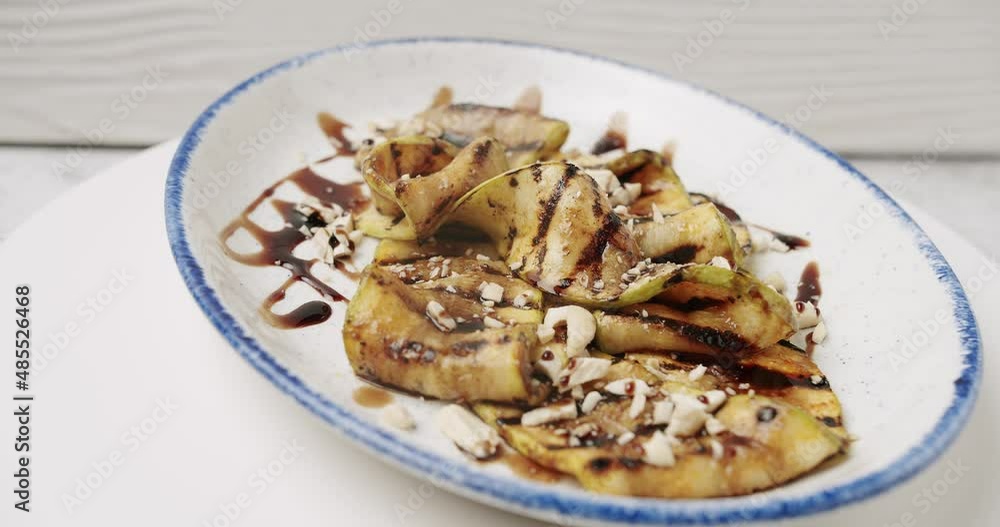 Tasty grilled zucchini on white background. Grilled zucchini with nuts, ready to serve in the restaurant. it rotates on the white plate. grilled courgette. Vegetarian dish. Close-up. ready for eat. Tasty grilled zucchini on white background. Grilled zucchini with nuts, ready to serve in the restaurant. it rotates on the white plate. grilled courgette. Vegetarian dish. Close-up. ready for eat.