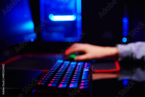 Teenager boy play computer video game in dark room, use neon colored rgb mechanical keyboard, workplace for cybersport gaming