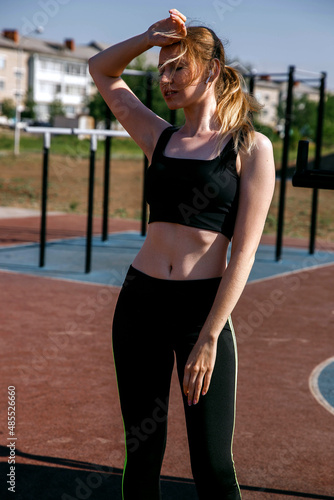 Young girl in a sports uniform on the street stand next to the uneven bars