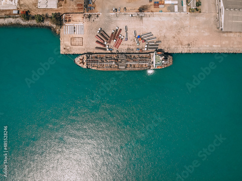 Drone view of the oil tanker at the quay, pumping fuel into numerous petrol trucks through gas pipes; technology concept.