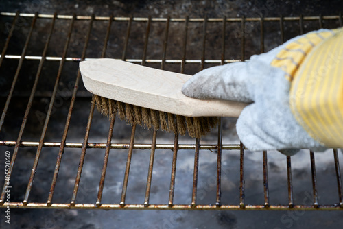 Wooden wire brush cleans dirty barbecue grill rust. Leather protection gloves. photo