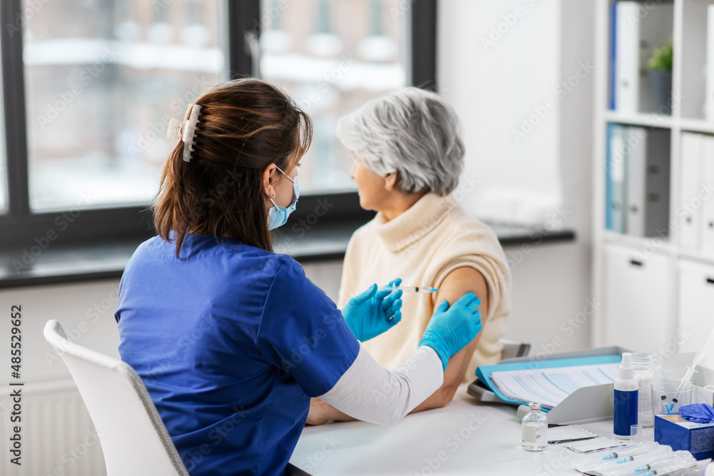 Obraz premium medicine, health and vaccination concept - doctor or nurse with syringe making vaccine or drug injection to senior woman at hospital