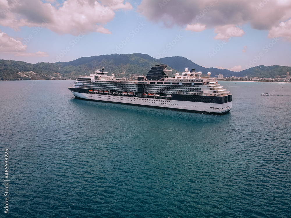 Luxurious black and white cruise liner in the harbor near the coastal European town, vast blue sea, pink clouds; drone shot, side view.