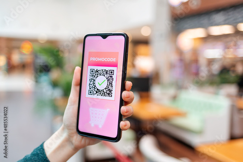 A female's hand holds a cellphone with a qr code for a discount in the internet store. The concept of online shopping and discounts