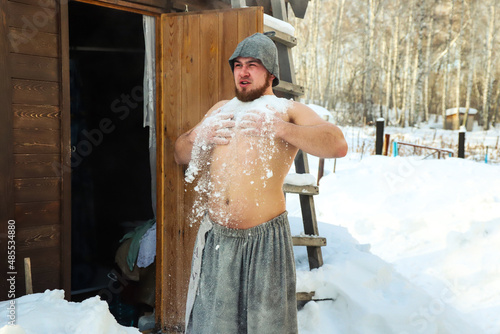 A man after sauna throwing snow on himself. Outdoors. Cold snowy winter