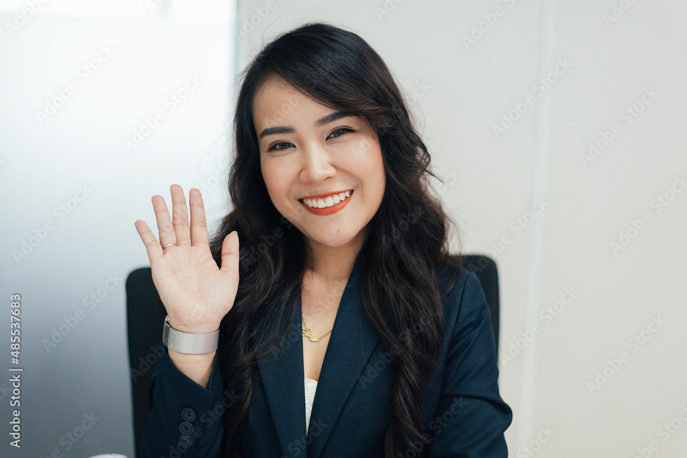 Portrait POV of Asian female employee waving hand to camera greeting to customer or colleagues on meeting video conference. cheerful telemarketer working in the office Portrait POV of Asian female employee waving hand to camera greeting to customer or colleagues on meeting video conference. cheerful telemarketer working in the office