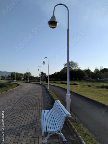 Fotografija View of a road with a white bench and a beautiful lamppost behind it