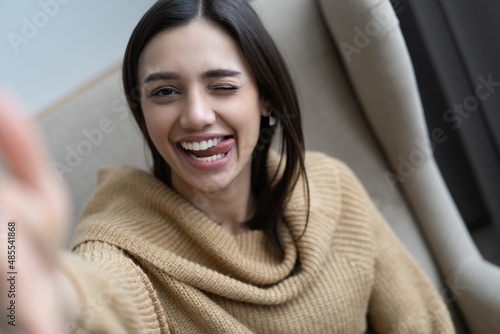 Image closeup of stylish woman 20s smiling while looking at camera and taking selfie photo in living room.