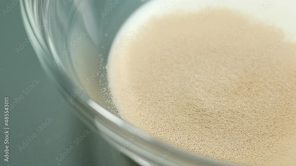 Macro shot of pouring yeasts into glass bowl with milk and sugar