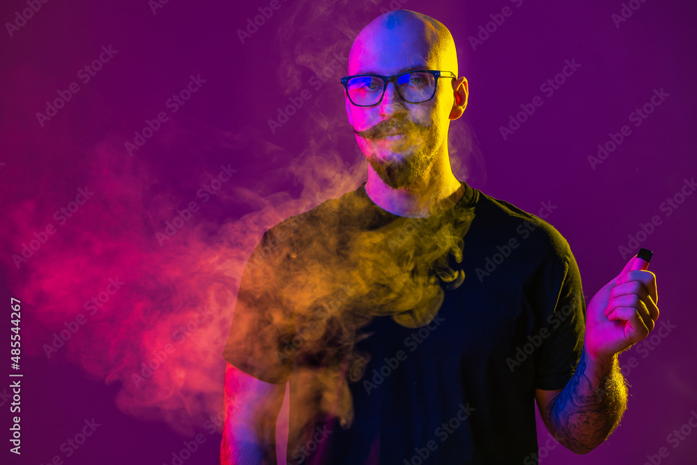 Adult person vaping in studio with colored lights. man using electronic cigarette and exhaling large amounts of vapor Adult person vaping in studio with colored lights. man using electronic cigarette and exhaling large amounts of vapor