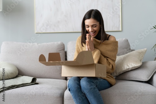 Happy young woman sit on couch room unpack cardboard box buying goods on Internet. shopping online, delivery concept photo