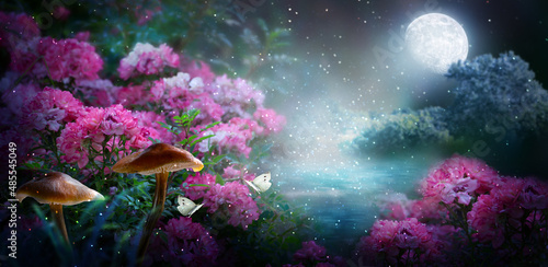 Fantasy magical fairy tale landscape with enchanted forest lake  fabulous fairytale blooming pink rose flower garden  mushrooms and two butterflies on mysterious background and glowing moon in night.