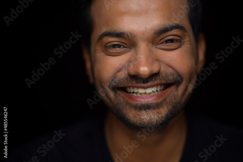 Close-up portrait of a happy young man against dark background