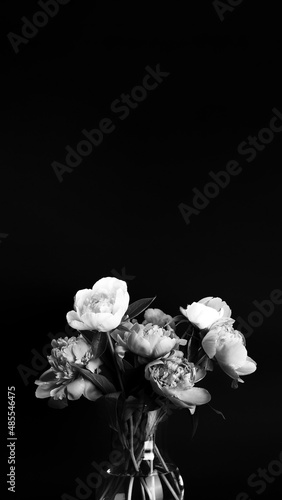 Bouquet of peonies in glass vase on black background with copy space vertical banner. Black and white photo. Floral card, poster design. Selective focus
