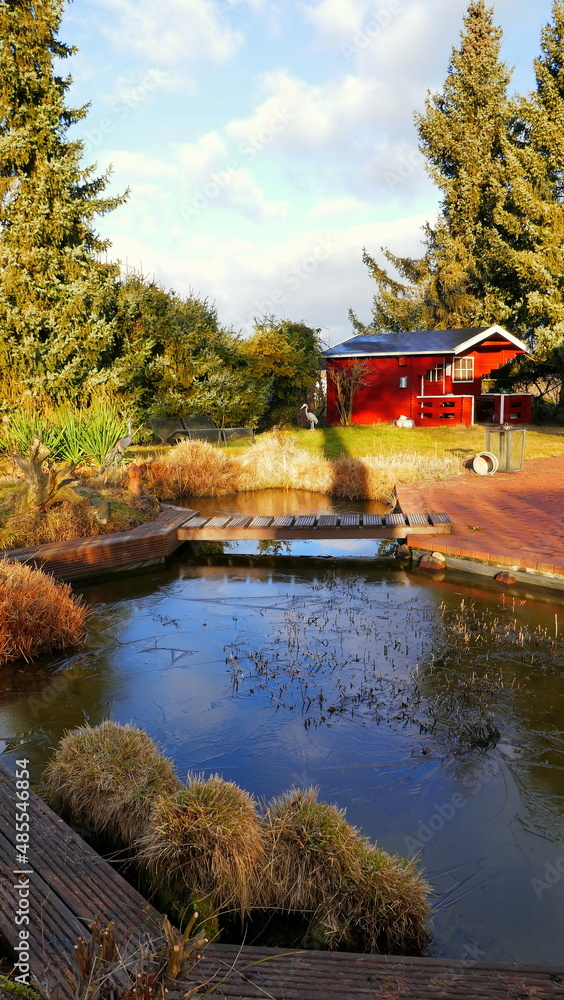 malerischer Teich mit Brücke und roter Terrasse mit Gartenhaus und