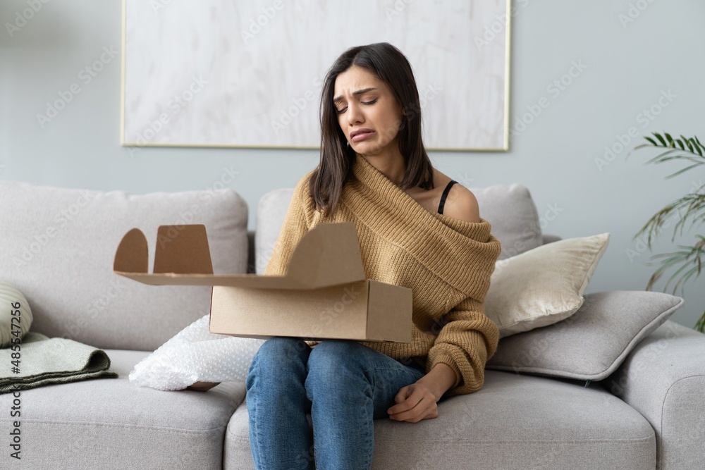 Angry confused woman unpacking parcel, wrong or broken online store order. Bad delivery service Angry confused woman unpacking parcel, wrong or broken online store order. Bad delivery service