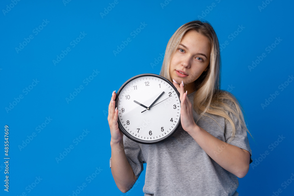 Beautiful teen girl holding wall clock over blue background Beautiful teen girl holding wall clock over blue background