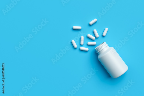 Plastic medical container and white capsule pills on blue background copy space top view. Medicine and health concept. 3d rendering.