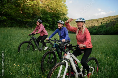 Happy active senior women friends cycling together outdoors in nature.