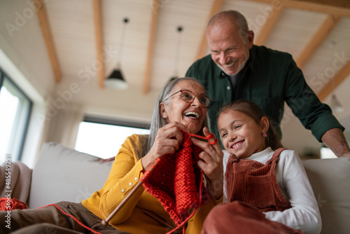 Grandmother sitting on sofa and teaching her granddaughter how to knit indoors at home.