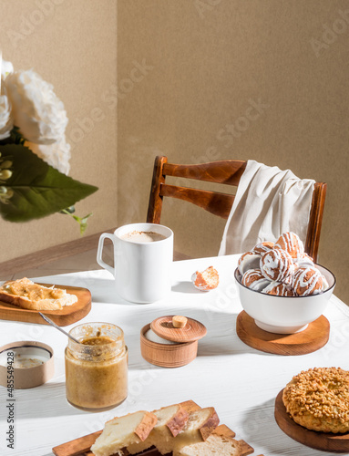 Morning romantic breakfast. On a white wooden table: In a mug of hot coffee (steam comes out of it), cakes, cookies, bread, sugar. Nearby is a chair with a napkin. Breakfast concept.