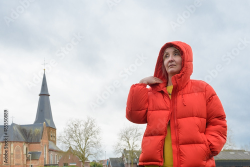 Woman in a red jacket. Portrait of woman against an old catholic church and cloudy sky. copy space