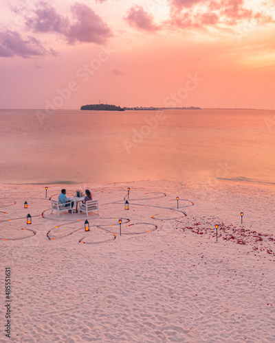 Honeymoon couple at private luxury romantic dinner on tropical beach in Maldives. Seaside, amazing island shore with candles and flower petals. Romantic love dinner destination dining beautiful aerial