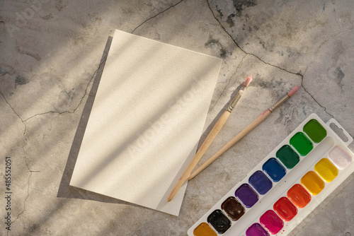 A sheet of paper for drawing, a watercolor palette and brushes on a concrete table. photo