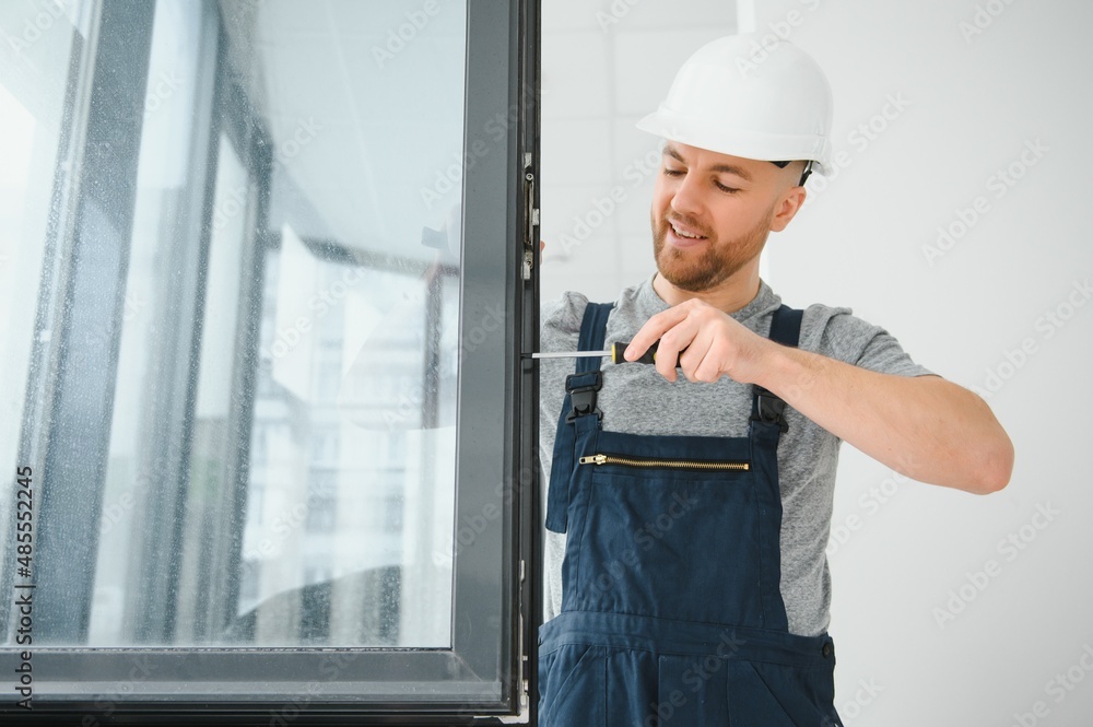 Construction worker repairing plastic window with screwdriver indoors, space for text. Banner design Construction worker repairing plastic window with screwdriver indoors, space for text. Banner design