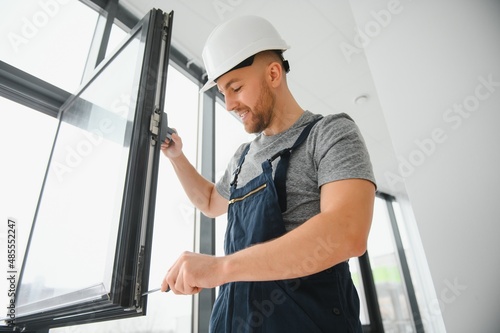 Workman in overalls installing or adjusting plastic windows in the living room at home