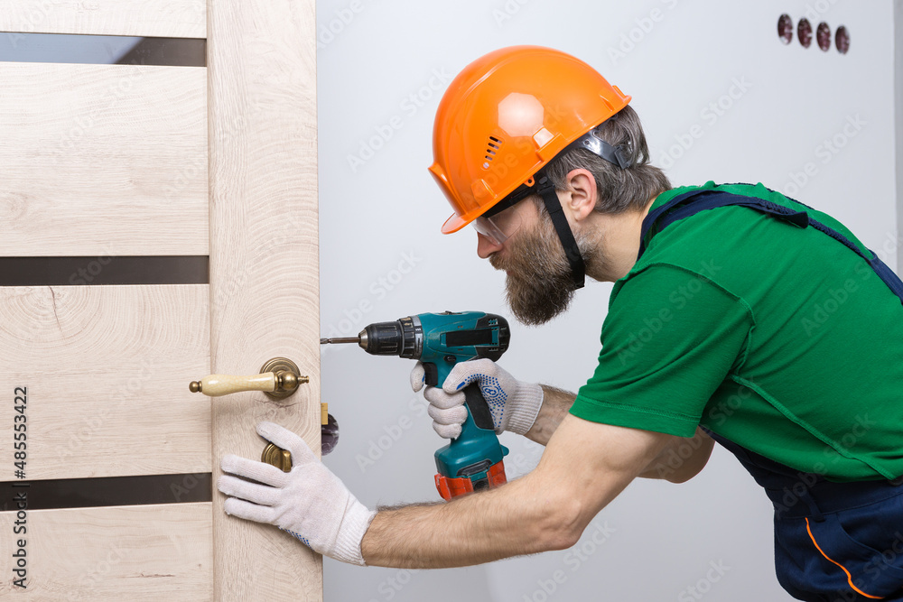 A male locksmith installs a door in an apartment. The guy works with a screwdriver. A male locksmith installs a door in an apartment. The guy works with a screwdriver.