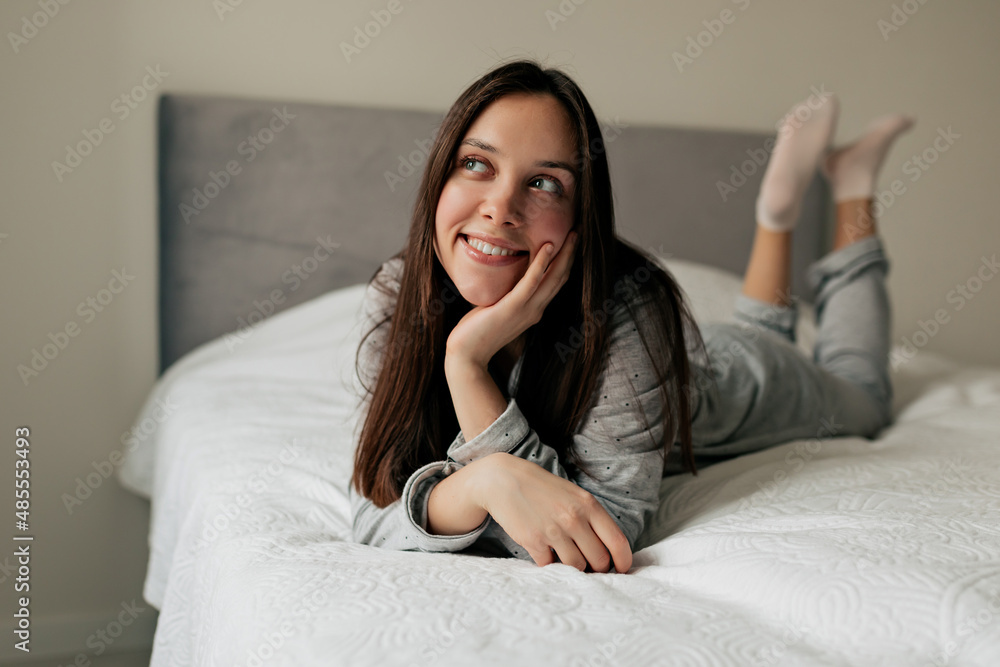 Wonderful dreamy girl with dark hair is lying on the bed with happy smile in romantic mood. Charming lady woke up in the morning and planning her day Wonderful dreamy girl with dark hair is lying on the bed with happy smile in romantic mood. Charming lady woke up in the morning and planning her day