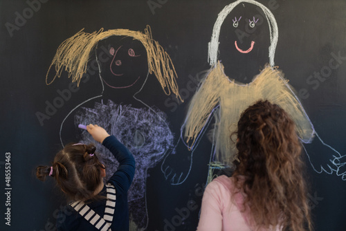 Rear view of group of little girls drawing with chalks on blackboard wall indoors in playroom.