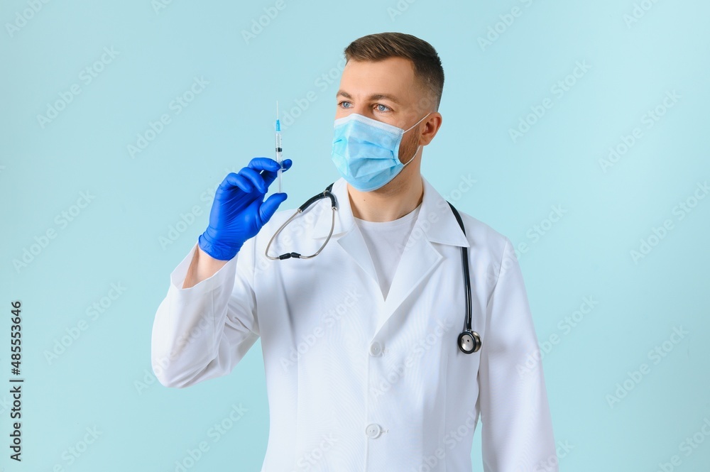 young doctor in medical mask and white coat with stethoscope holding syringe isolated on blue young doctor in medical mask and white coat with stethoscope holding syringe isolated on blue