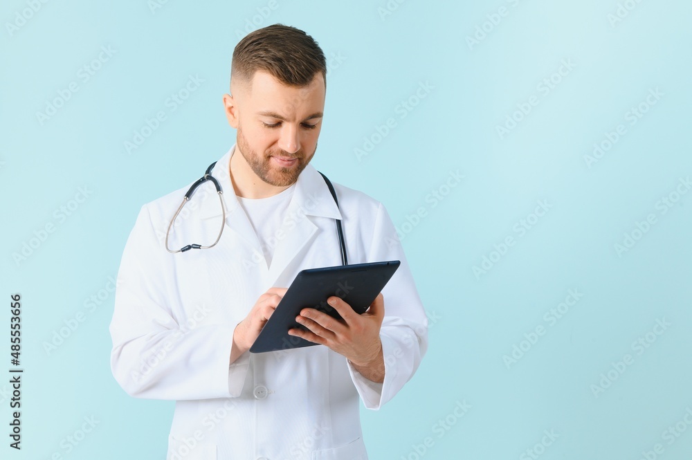 Medic in white robe, looking straight at camera with positive smile, holding tablet computer next to chest while working in hospital, isolated on blue background Medic in white robe, looking straight at camera with positive smile, holding tablet computer next to chest while working in hospital, isolated on blue background