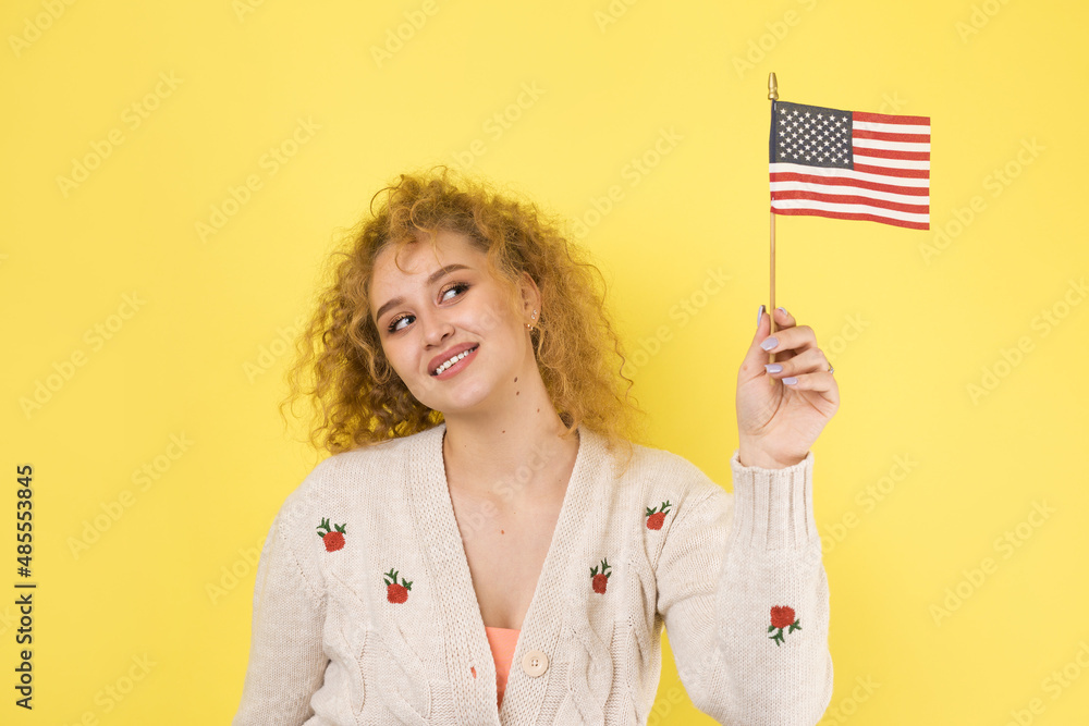 A young happy girl with a smile on her face holds an American flag in her hands. Symbol of patriotism and freedom. A young happy girl with a smile on her face holds an American flag in her hands. Symbol of patriotism and freedom.