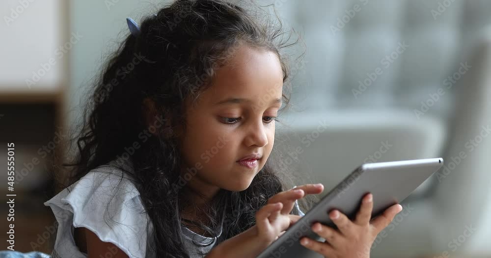Generation Z and modern wireless tech, parental control software, apps usage concept. Close up pretty little Indian girl using digital tablet, play games on-line, spend time on internet alone at home Generation Z and modern wireless tech, parental control software, apps usage concept. Close up pretty little Indian girl using digital tablet, play games on-line, spend time on internet alone at home