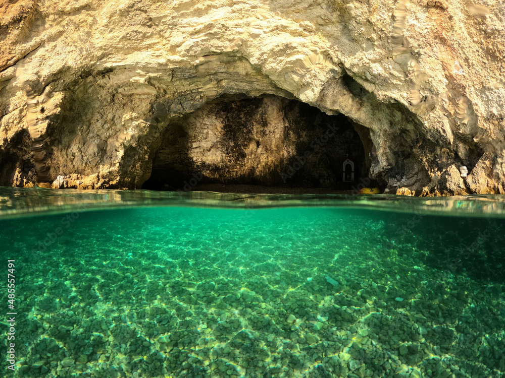 Underwater split photo of small white rock cave with crystal clear emerald sea and chapel of Agios Nikolaos built inside the cave, Desimi beach, Lefkada island, Ionian, Greece