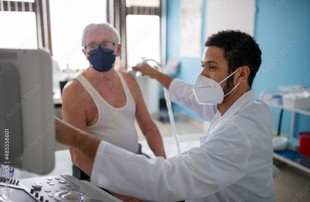 Young doctor is examining senior patient by using an ultrasound equipment in clinic.