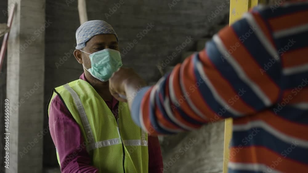 shoulder shot of man checking body tempreture of labour with medical face mask at construction site - concept of covid19 precaution, back to work and blue collar jobs. shoulder shot of man checking body tempreture of labour with medical face mask at construction site - concept of covid19 precaution, back to work and blue collar jobs.