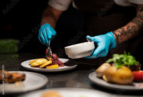 Chef's hands in gloves serving and decorating meal in restaurant kitchen