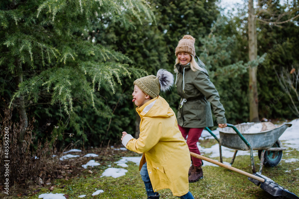 Boy with Down syndrome with his grandmother working in garden in winter together.