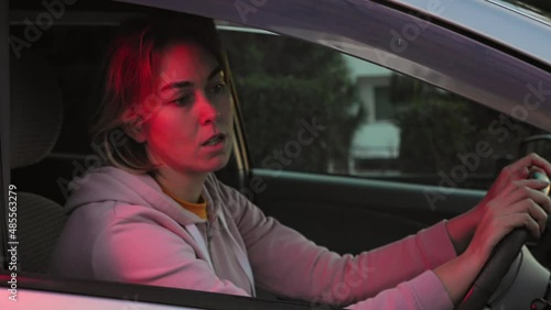 A young woman is sitting behind the wheel of a right-hand drive car and nervously looks in the rearview mirror, waiting for a policeman. The police siren light is blinking. Speeding ticket. photo