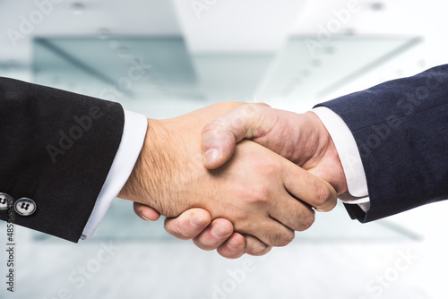 Handshake of two businessmen on the background of sunny modern furnished office, signing of a contract concept, close up