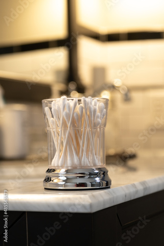 White Cotton Swabs in a Glass Container on the Edge of a Bathroom Vanity